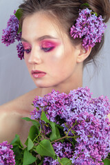 Portrait of a young girl in the studio with lilac flowers on her head, close-up. Creative beautiful make-up in doll style with lilac flowers on the head close-up.