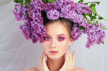 Portrait of a young girl in the studio with lilac flowers on her head, close-up. Creative beautiful make-up in doll style with lilac flowers on the head close-up.