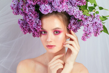 Portrait of a young girl in the studio with lilac flowers on her head, close-up. Creative beautiful make-up in doll style with lilac flowers on the head close-up.