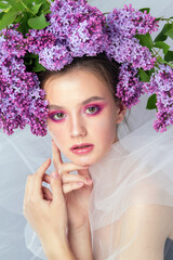 Portrait of a young girl in the studio with lilac flowers on her head, close-up. Creative beautiful make-up in doll style with lilac flowers on the head close-up.