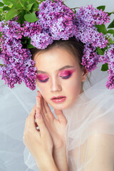 Portrait of a young girl in the studio with lilac flowers on her head, close-up. Creative beautiful make-up in doll style with lilac flowers on the head close-up.