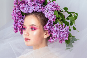 Portrait of a young girl in the studio with lilac flowers on her head, close-up. Creative beautiful make-up in doll style with lilac flowers on the head close-up.