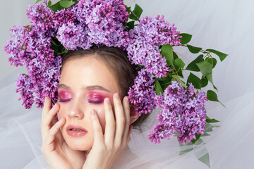 Portrait of a young girl in the studio with lilac flowers on her head, close-up. Creative beautiful make-up in doll style with lilac flowers on the head close-up.
