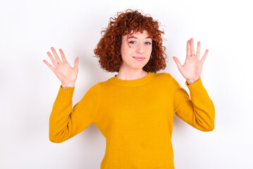 Maybe yes or no. Doubtful young redhead girl wearing yellow sweater over white background shrugs shoulders in bewilderment, tries to make decision puzzled what he wants.
