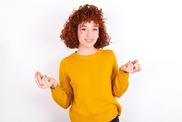 young redhead girl wearing yellow sweater over white background, making money gesture.