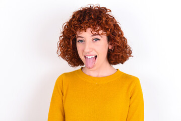 young redhead girl wearing yellow sweater over white background with happy and funny face smiling and showing tongue.