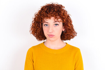 young redhead girl wearing yellow sweater over white background frowning his eyebrows being displeased with something.