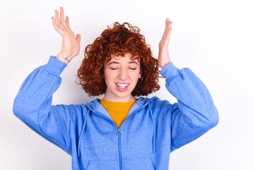 young redhead girl wearing blue jacket over white background goes crazy as head goes around feels...