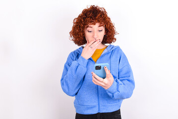 young redhead girl wearing blue jacket over white background being deeply surprised, stares at...