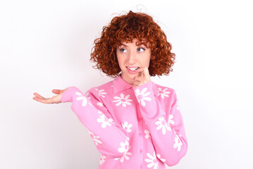 Positive young redhead girl wearing pink floral t-shirt over white background advert promo touches teeth with finger.