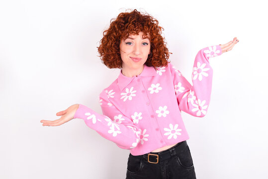 Careless attractive young redhead girl wearing pink floral t-shirt over white background shrugging shoulders, oops.