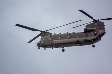 Fototapeta na wymiar close up of an RAF Chinook tandem-rotor CH-47 helicopter flying fast and low in a cloudy blue grey sky on a military battle exercise, Wilts UK