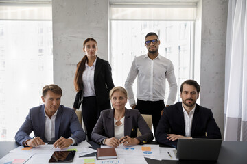 Group portrait of five confident serious diverse business people employees managers of different ages in formal wear posing together in modern workplace, professional career, teamwork concept.