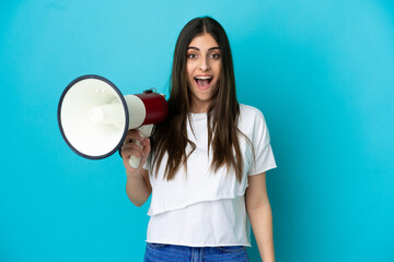 Young caucasian woman isolated on blue background holding a megaphone and with surprise expression