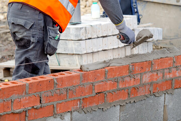 Bricklayer laying bricks on mortar on new residential house construction
