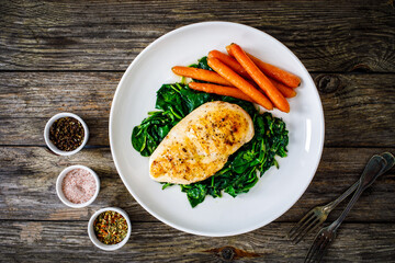 Fried chicken breast with spinach and carrots on wooden table