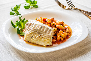 Fish dish - fried cod fillet with fresh fruit salsa on white table
