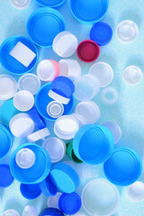 Colorated plastic bottle caps on a light blue background. View from above.

