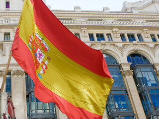 Spanish flag waving against classical buildings in Gran Via street in Madrid, Spain