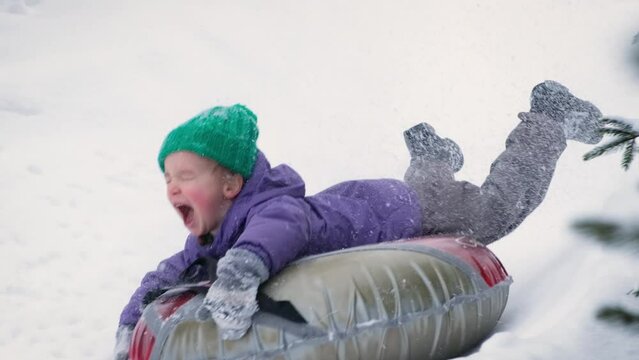 Snow tubing. Funny little child boy riding on inflatable tube. Kid sledding slide down hill. Winter fun activity outdoor.