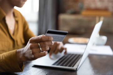 Female hand holding credit card at laptop close up. Young Black customer, shopaholic woman making payment for purchase on Internet, bank transactions, mortgage fees, buying on shop websites
