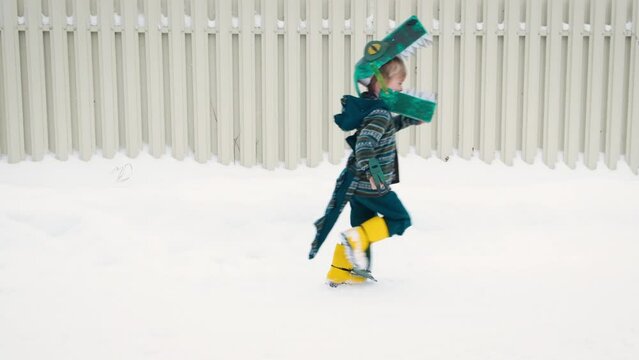 Funny playful little child boy in homemade cardboard textile dinosaur or crocodile costume running on snowy road.