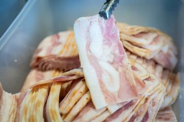 Smoked bacon slices on tongs.