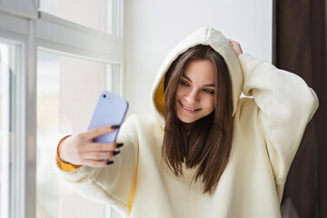 Happy female blogger taking selfie portrait on smartphone camera for social media posting, cheerful teenage girl talking on video call with family or friends via mobile phone.Soft selective focus.