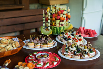 The buffet at the reception. Assortment of canapes on wooden board. Banquet service. Catering, snacks with different types of cheese and meat. Party Concept.