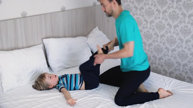 Father massages his little son. Dad stretches legs of his child boy. Family sports warm-up.