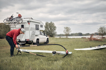 Windsurfer and camper packing and unpacking from a car in nature.