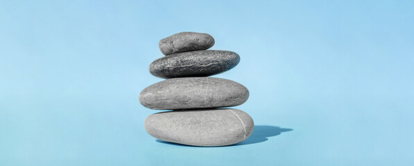 Fototapeta na wymiar The balancing cairn - symbol of harmony, tranquility and relaxation, concept of meditation. Stack of spa hot stones. Balanced pebble stones for spa treatments on blue background.