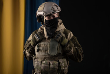 a male soldier in a military uniform and helmet on the background of the national flag of Ukraine