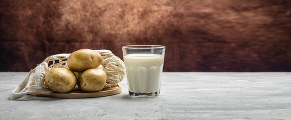 vegan potato milk in glass and raw potato. Alternative plant based milk. Healthy food trend. Healthy, clean eating. Vegan or gluten free diet. Long banner format. top view