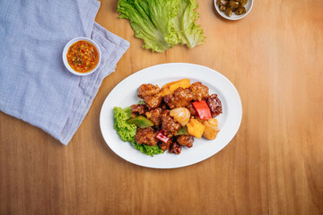 Chinese food Sweet and Sour Pork in a dish with chili sauce, and king's salad leaf top view on wooden background