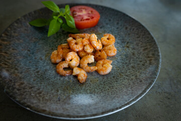 Delicious freshly cooked shrimp on a gray plate next to a tomato and basil. Free space to write.