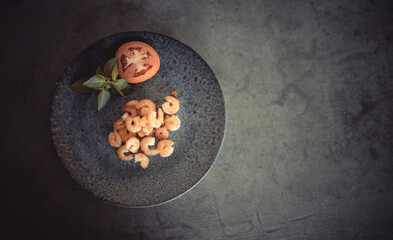 Delicious freshly cooked shrimp on a gray plate next to a tomato and basil. Free space to write.