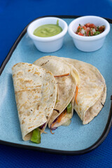 A plate of Mexican quesadilla with vegetables and cheese on a blue plate with guacamole and salsa