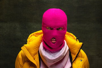 Studio shot of young anonymous man wearing pink balaclava and yellow down jacket, coat isolated on...