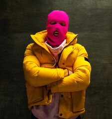 Studio shot of young anonymous man wearing pink balaclava and yellow down jacket, coat isolated on...