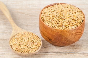 Gold flax seeds in a wooden bowl on a brown background.