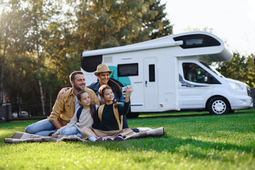 Happy young family with two children ltaking selfie with caravan at background outdoors. - obrazy, fototapety, plakaty