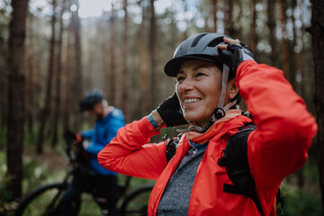 Senior couple bikers putting on cycling helmet outdoors in forest in autumn day. - Powered by Adobe