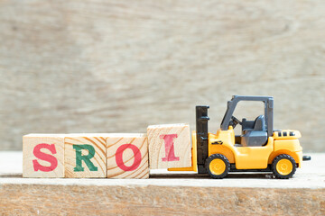 Toy forklift hold letter block I to complete word SROI (Abbreviation of Social Return on Investment) on wood background