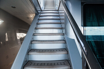 Access to the next floor of the yacht with a wooden staircase, railings and a closing hatch. Internal staircase on the yacht with handrails. Yacht interior with ladder.