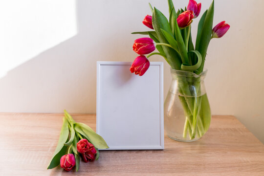 Portrait white picture frame mockup on wooden table. Modern vase with tulips.Scandinavian interior