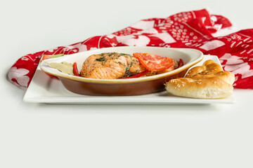 Baked salmon fillet with pita bread, cucumber, tomato in a dish isolated on colorful table cloth top view on grey background