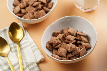 Nougat bites - sweet cocoa and hazelnut wheat puffed pillows - breakfast cereal in white bowls, glasses with milk on sunny orange background