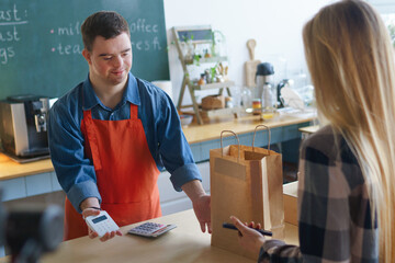 Cheerful young Down Syndrome waiter serving customer in take away restaurant, social inclusion...
