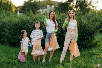 A group of adults and children together at sunset is engaged in garbage collection in the park....